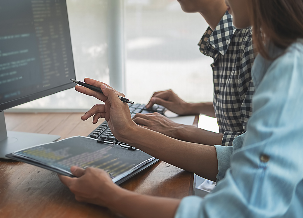 Zwei Mitarbeitende sitzen vor einem PC-Monitor